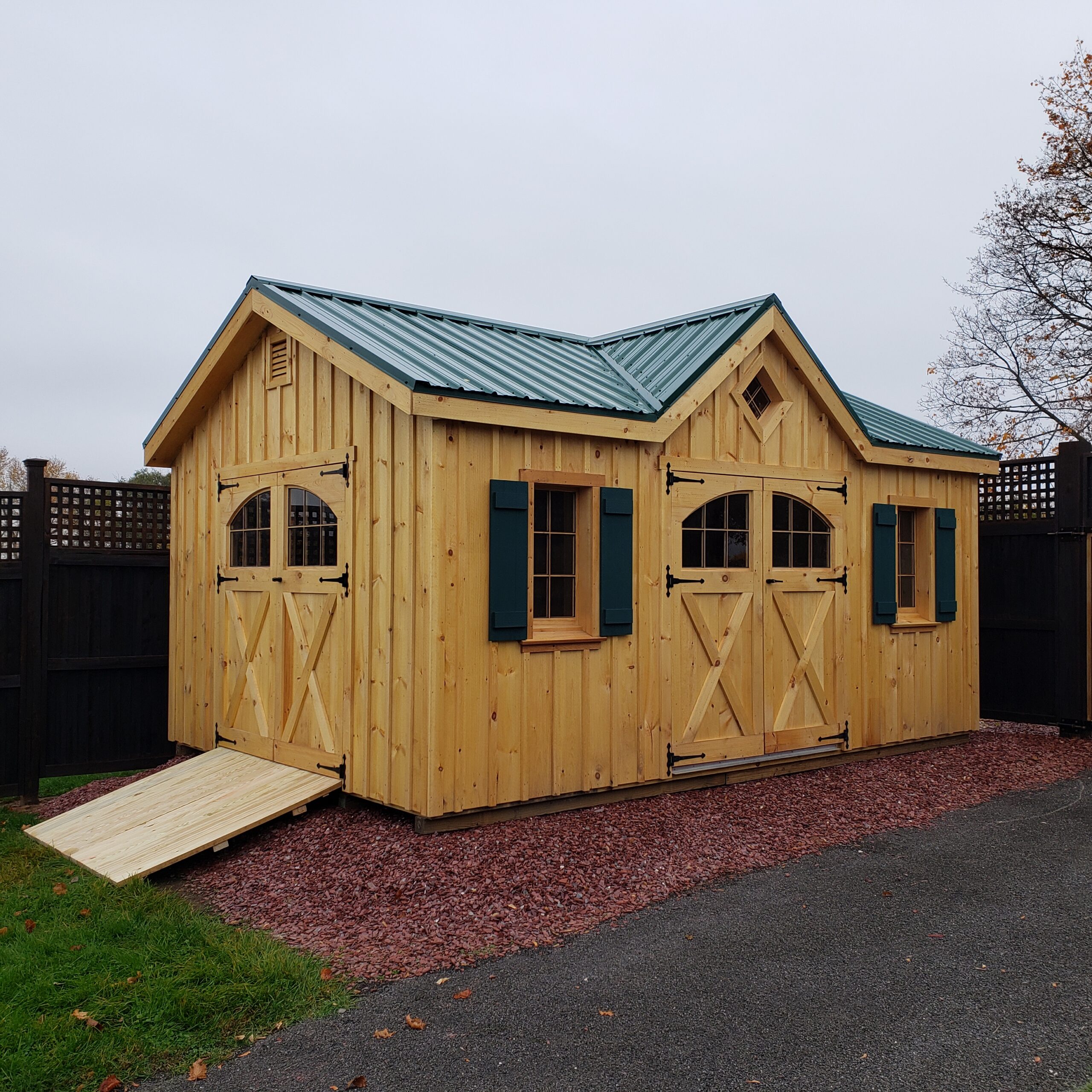 A board-and-batten A-frame wood shed built on a bed of mulch in a backyard.
