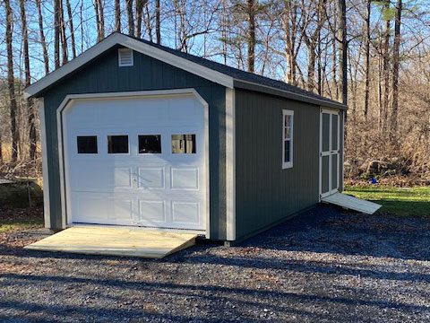 A blue garage set on a gravel driveway in a wooded area