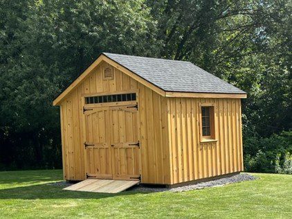 A pine shed in the middle of a yard with trees behind it